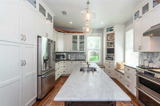 kitchen featuring pendant lighting, high end appliances, white cabinets, an island with sink, and light stone counters