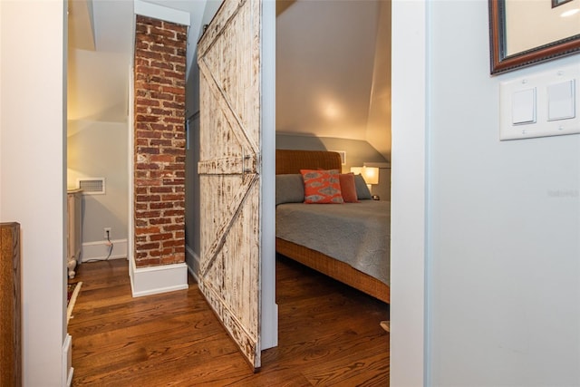 bedroom featuring a barn door, dark hardwood / wood-style floors, and vaulted ceiling