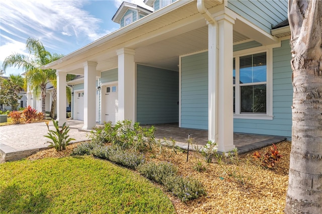 doorway to property with covered porch, decorative driveway, and a garage