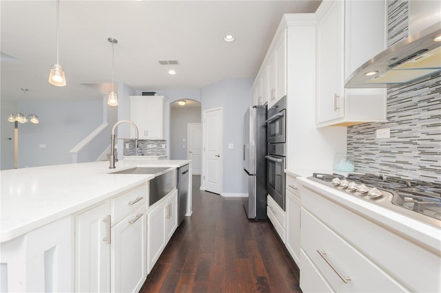 kitchen with white cabinets, wall chimney exhaust hood, stainless steel appliances, light countertops, and a sink