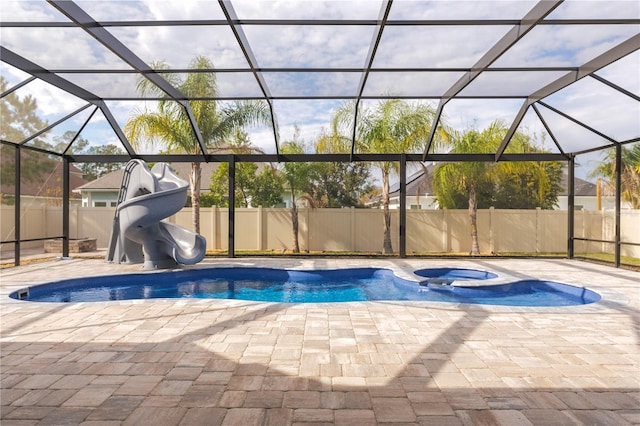 view of swimming pool featuring glass enclosure, a water slide, fence, a pool with connected hot tub, and a patio area