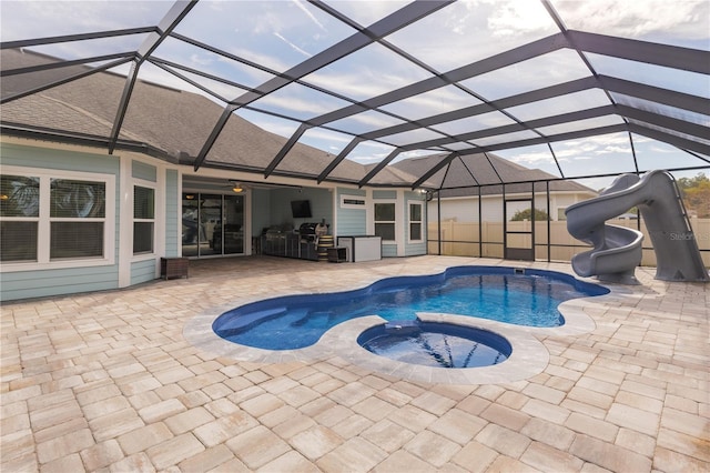 view of swimming pool with glass enclosure, a water slide, a patio area, and a pool with connected hot tub