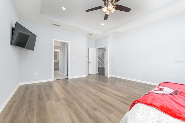 bedroom with wood finished floors, a raised ceiling, visible vents, and baseboards