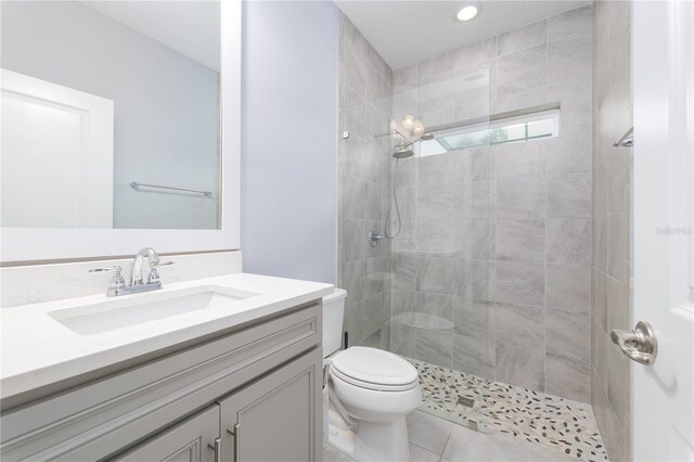 full bath with tiled shower, vanity, toilet, and tile patterned floors