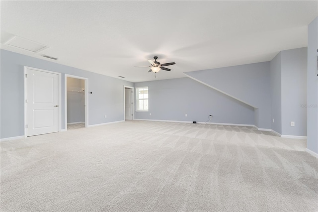 empty room with attic access, baseboards, ceiling fan, and light colored carpet