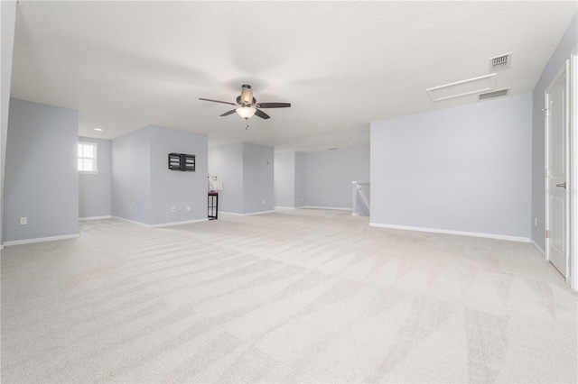 unfurnished living room featuring light colored carpet, visible vents, attic access, a ceiling fan, and baseboards