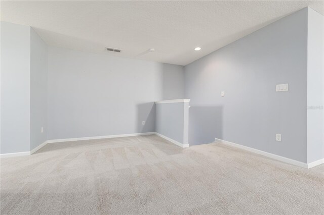 unfurnished room featuring a textured ceiling, recessed lighting, light colored carpet, visible vents, and baseboards