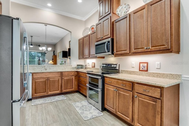 kitchen with hanging light fixtures, light stone counters, appliances with stainless steel finishes, ceiling fan with notable chandelier, and ornamental molding