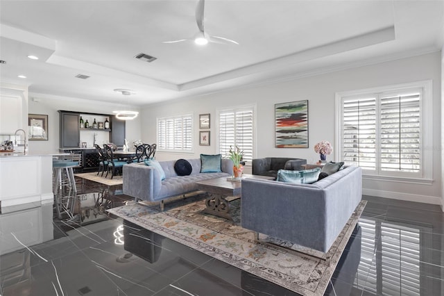 living room featuring a raised ceiling, ceiling fan, and crown molding