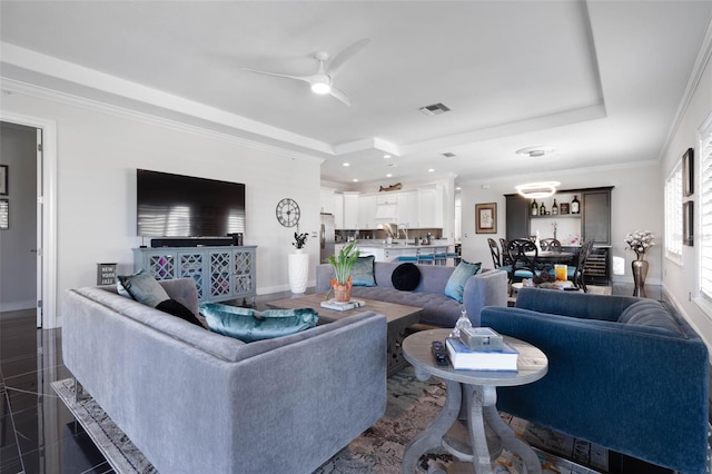 tiled living room with a raised ceiling, ceiling fan, and crown molding