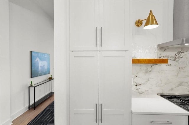 interior space featuring backsplash, wall chimney exhaust hood, light hardwood / wood-style floors, white cabinetry, and gas cooktop