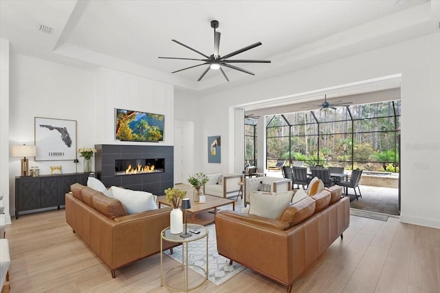 living room with a raised ceiling, light wood-type flooring, and a tile fireplace