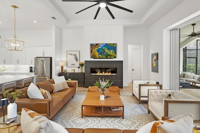 living room with a fireplace, light wood-type flooring, a tray ceiling, and a notable chandelier