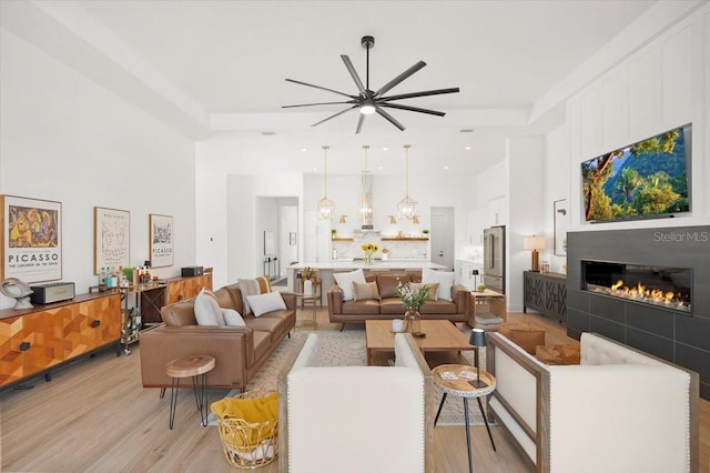 living room with a tile fireplace, ceiling fan, and light wood-type flooring