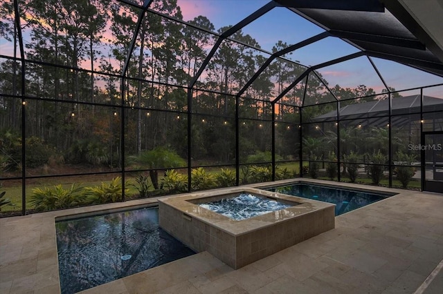 pool at dusk with an in ground hot tub, glass enclosure, and a patio area