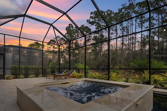 pool at dusk featuring glass enclosure and a patio