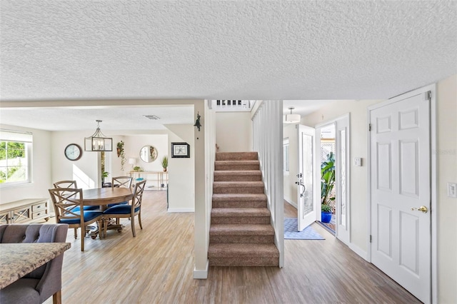 entryway with light hardwood / wood-style flooring, a textured ceiling, and a notable chandelier