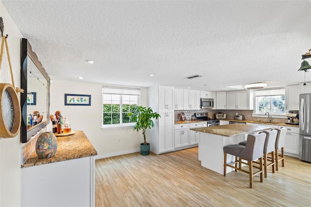 kitchen with a kitchen bar, stainless steel appliances, sink, white cabinets, and a center island