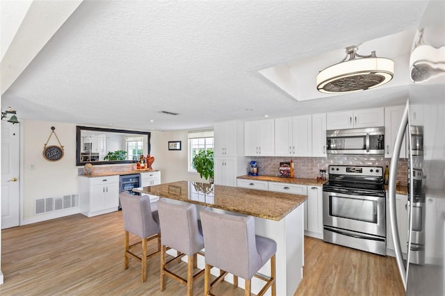 kitchen with white cabinets, a center island, stainless steel appliances, and dark stone counters