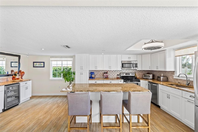 kitchen with appliances with stainless steel finishes, wine cooler, sink, a center island, and white cabinetry