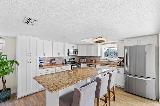 kitchen with a center island, sink, stainless steel appliances, light stone counters, and white cabinets