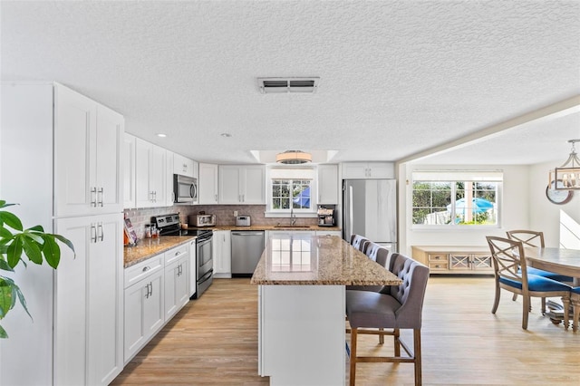 kitchen featuring light stone counters, stainless steel appliances, white cabinets, a center island, and a breakfast bar area