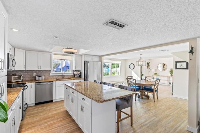 kitchen featuring stainless steel appliances, sink, stone countertops, white cabinetry, and a kitchen island