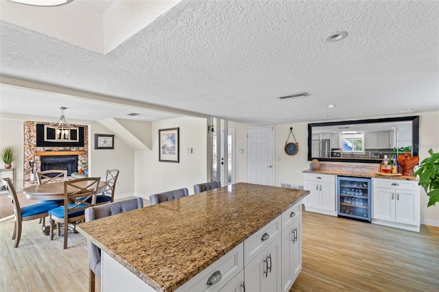 kitchen with white cabinets, a kitchen island, beverage cooler, and light stone counters