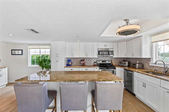 kitchen with white cabinets, a kitchen island, sink, and appliances with stainless steel finishes