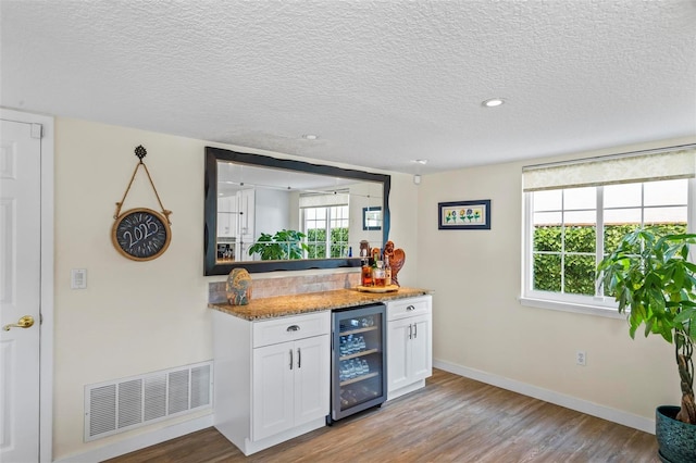 kitchen with light stone countertops, wine cooler, a textured ceiling, light hardwood / wood-style flooring, and white cabinetry