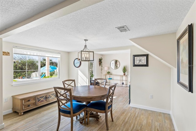 dining space with light hardwood / wood-style floors, a textured ceiling, and a notable chandelier