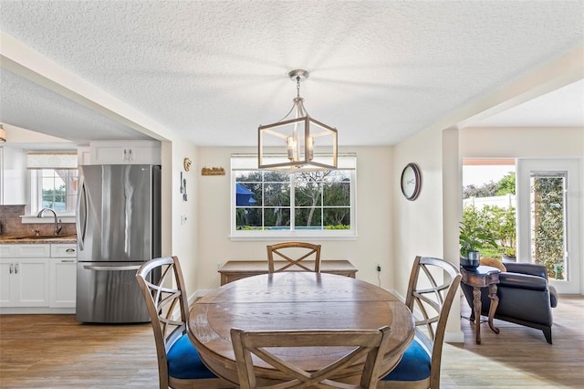 dining area with sink, light hardwood / wood-style flooring, a textured ceiling, and a notable chandelier