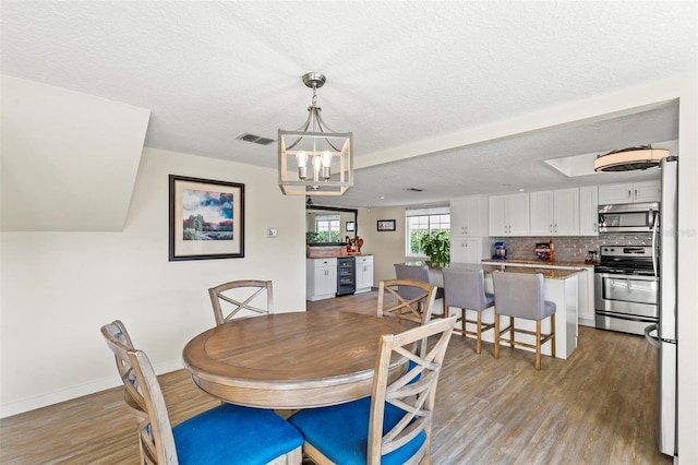 dining space with wine cooler, a textured ceiling, light hardwood / wood-style flooring, and a notable chandelier