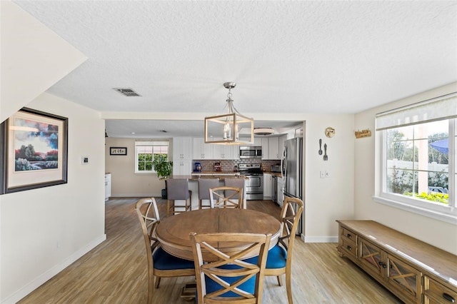 dining space featuring a chandelier, a textured ceiling, and light hardwood / wood-style flooring