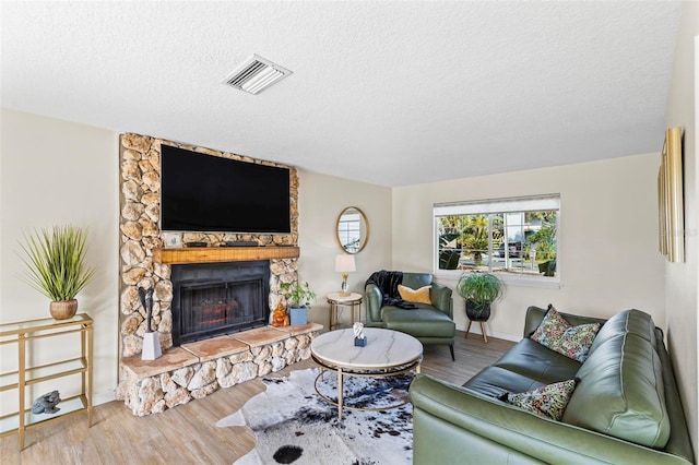 living room with hardwood / wood-style floors, a stone fireplace, and a textured ceiling