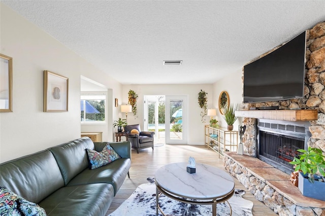 living room with a stone fireplace, light wood-type flooring, and a textured ceiling