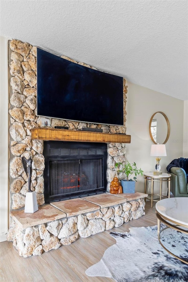 room details featuring wood-type flooring, a textured ceiling, and a stone fireplace