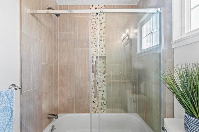 bathroom featuring toilet and bath / shower combo with glass door