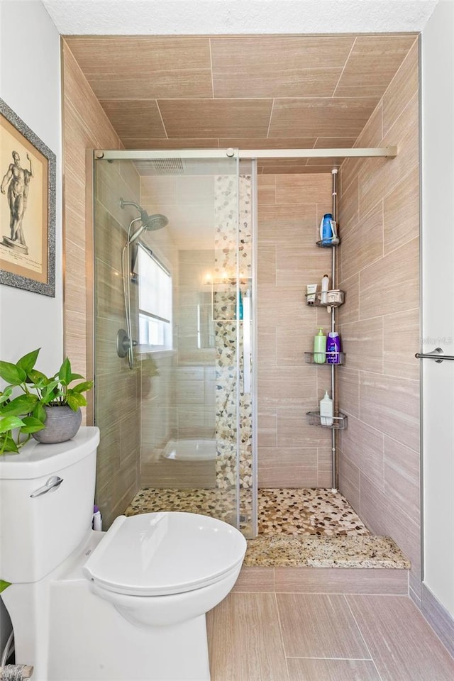 bathroom featuring a shower with door and toilet