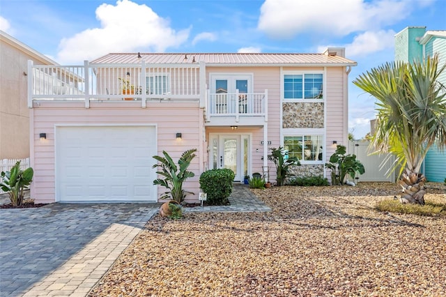 view of front of house featuring decorative driveway, fence, french doors, metal roof, and a balcony