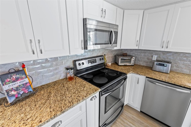 kitchen with light stone counters, tasteful backsplash, appliances with stainless steel finishes, and white cabinets