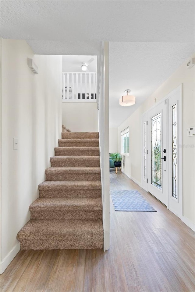 foyer entrance featuring stairway, a textured ceiling, baseboards, and wood finished floors