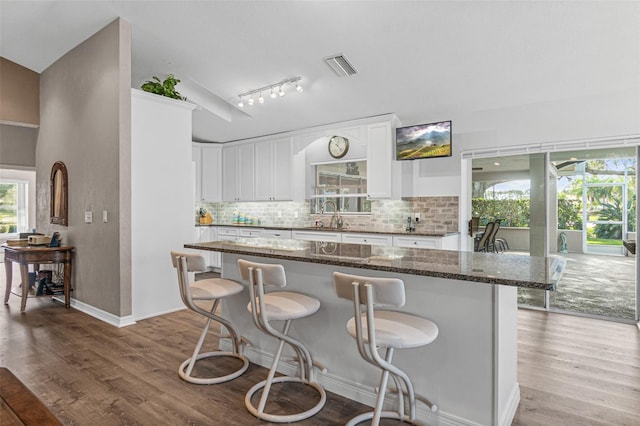 kitchen with dark stone countertops, a breakfast bar area, light hardwood / wood-style floors, sink, and white cabinetry