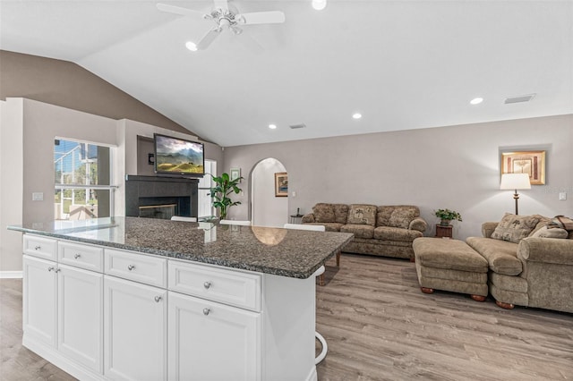 kitchen featuring white cabinetry, a center island, a tiled fireplace, light wood-type flooring, and dark stone counters