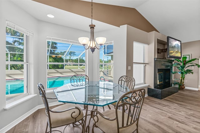 dining area featuring a tile fireplace, an inviting chandelier, vaulted ceiling, and wood-type flooring