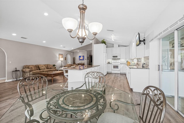 dining space with sink, vaulted ceiling, a notable chandelier, and light hardwood / wood-style flooring