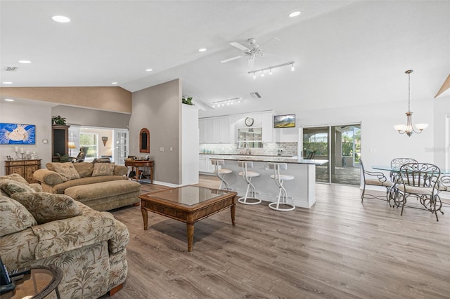 living room with light hardwood / wood-style floors, vaulted ceiling, and ceiling fan with notable chandelier