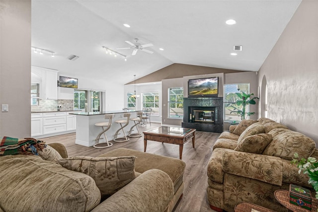 living room with lofted ceiling, a tile fireplace, ceiling fan, and light hardwood / wood-style flooring