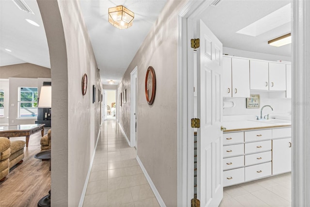 hallway with sink, lofted ceiling with skylight, and light tile patterned floors