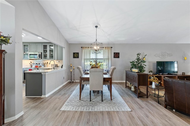 dining area featuring sink, light hardwood / wood-style flooring, lofted ceiling, and a notable chandelier